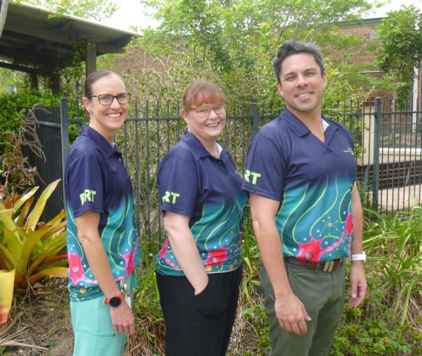 One male and two female health care workers standing near garden