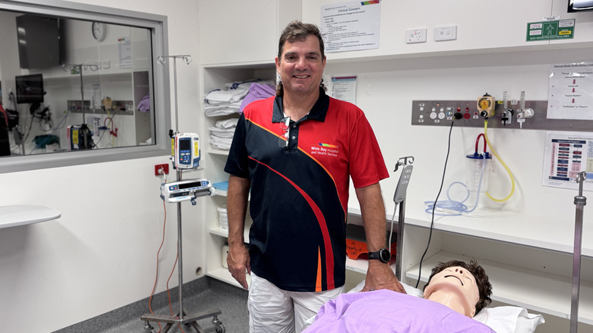 Image of male nurse standing beside bed with mannequin used for simulation training 