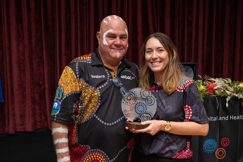 Female health care worker receiving award from First Nations representative.