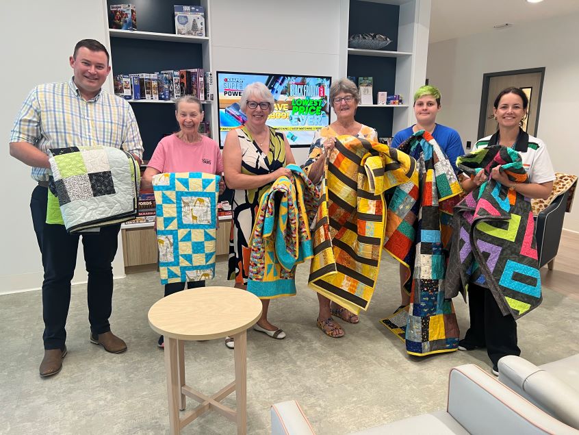 Group of quilters holding gifts of quilts for mental health spaces