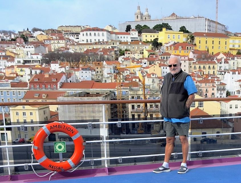 Man standing on deck of cruise ship with buildings in the background