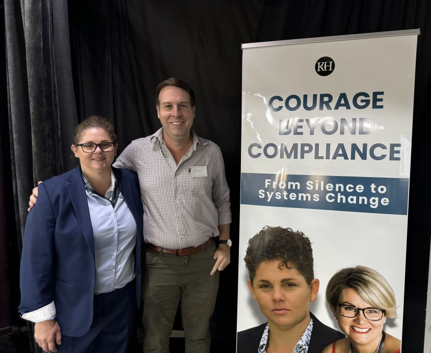 Man and woman standing next to a pull up banner reading Courage beyond compliance
