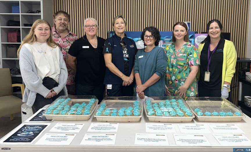 Group of healthcare workers standing behind table of blue iced cupcakes